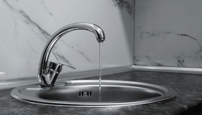 Running tap water in stainless steel sink highlighting risk of hidden drain leaks